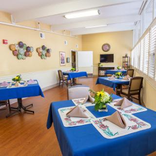 A cozy dining area with blue tables set for a meal, featuring decorative wall art and warm lighting.