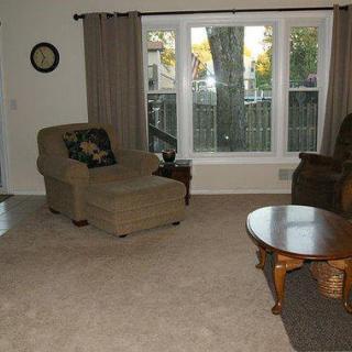 A cozy living room with an armchair, sofa, coffee table, and a large window with curtains.