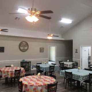 A cozy dining area with round tables covered in checkered tablecloths and ceiling fans overhead.