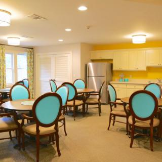 A brightly colored dining room with teal-backed chairs and a connected kitchen area.