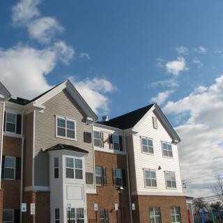 A modern apartment building under a bright blue sky with scattered clouds.