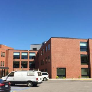 A brick building with large windows in a parking lot under a clear blue sky.