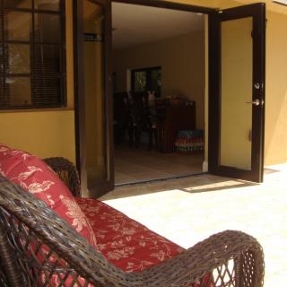 A cozy wicker chair on a sunlit patio, facing an open door leading to the interior of a home.