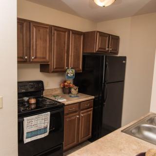A compact apartment kitchen with wooden cabinets, a stove, and a refrigerator.