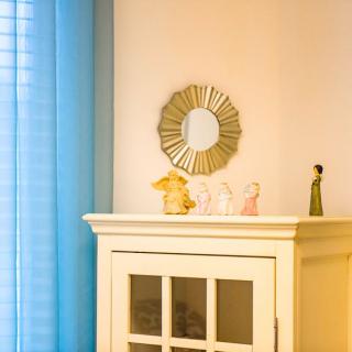 A cozy room corner with a cabinet topped by decorative figurines and a round mirror, set against blue curtains.