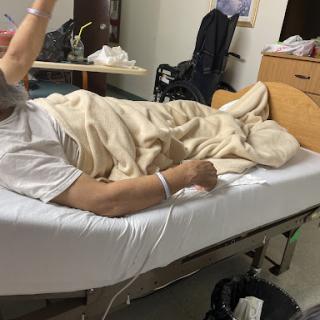 A patient resting in a hospital bed, covered with a blanket and connected to medical equipment.