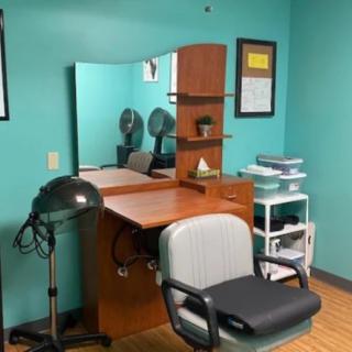 A hairstyling station in a salon featuring a mirror, chair, and hair drying equipment.