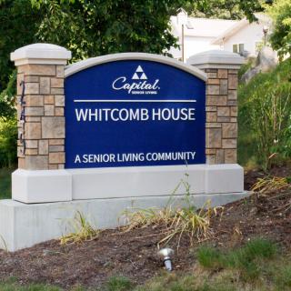A sign for Whitcomb House, a senior living community, surrounded by landscaping.