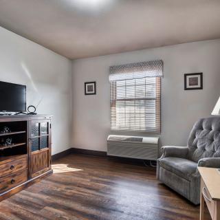 A cozy living room with a TV stand, armchair, and window on a hardwood floor.