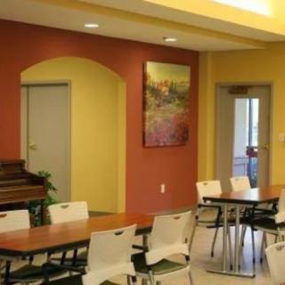 A bright dining area with colorful walls, featuring tables and chairs, a decorative painting, and doorways.