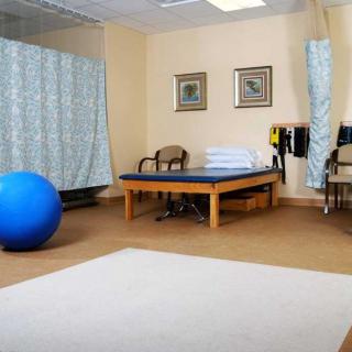 A physical therapy room with a treatment table, exercise equipment, and chairs.