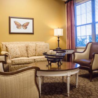 A cozy living room with a sofa, armchairs, and a coffee table, warmly lit by a lamp near the window.
