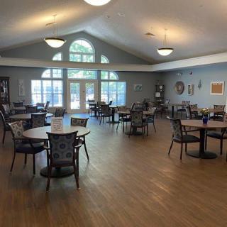 A spacious dining area with several tables and chairs, featuring large windows and wooden flooring.