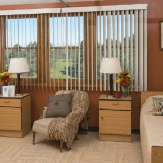 A cozy bedroom with large windows, featuring a bed, chair, nightstands, and lamps.