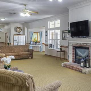 A cozy living room with sofas, a television above the fireplace, and ample natural light through the windows.