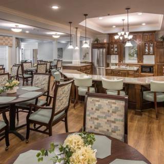 A spacious dining area with wooden flooring, featuring elegantly arranged tables and chairs near an open kitchen.