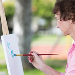 A woman painting on a canvas outside.