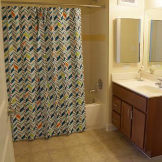 A bathroom featuring a colorful chevron-patterned shower curtain, a sink with a wooden cabinet, and two mirrors above the sink.