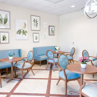A modern waiting room with blue seating, wooden tables, botanical artwork, and potted plants.