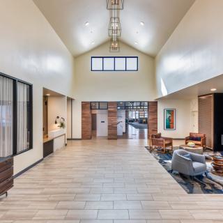 A modern and spacious lobby with a high ceiling, featuring comfortable seating and wood flooring.
