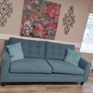 A cozy living room setup featuring a teal sofa with matching pillows, complemented by a colorful abstract painting and elegant wall decorations.