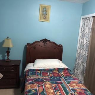 A cozy bedroom with a single bed, colorful bedspread, and a nightstand with a lamp against a blue wall.