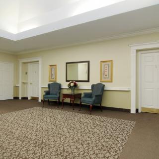 A hallway with a seating area featuring two chairs, a table, and a mirror on the wall.