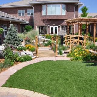 A beautifully landscaped garden featuring a small wooden bridge, pergola, and well-maintained lawn.