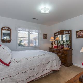 A cozy bedroom with a neatly made bed, wooden dresser, mirrors, and soft lighting.