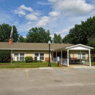 A single-story suburban building with a driveway and surrounding trees under a partly cloudy sky.