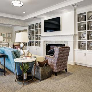 A cozy living room featuring comfortable seating, a television above the fireplace, and neatly organized shelves.