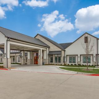 A modern building with a covered entrance and spacious driveway under a partly cloudy sky.