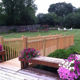 A serene backyard with a wooden deck, colorful flowers, and a fenced garden area.