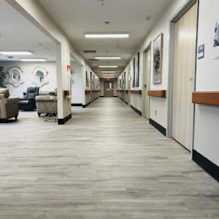 A view of a well-lit hallway in a healthcare facility, featuring seating areas and doors along the sides.