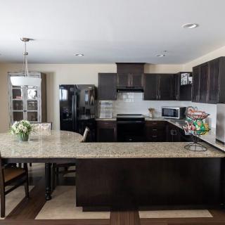 A modern kitchen with dark cabinets and granite countertops, featuring a dining area and appliances.