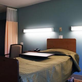 A hospital room with a single bed and overhead lighting.