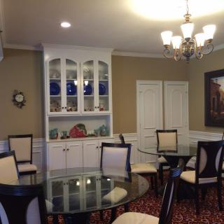 A well-decorated dining room featuring glass tables, upholstered chairs, a chandelier, and built-in cabinetry displaying decorative items.