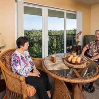 Two seniors relaxing and conversing in a cozy seating area with a scenic balcony view.