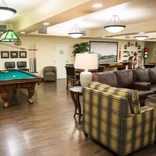 A cozy lounge and game room featuring a billiards table, comfortable seating, and warm lighting.
