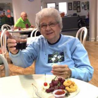 An elderly woman raises a glass while enjoying a meal at a restaurant.