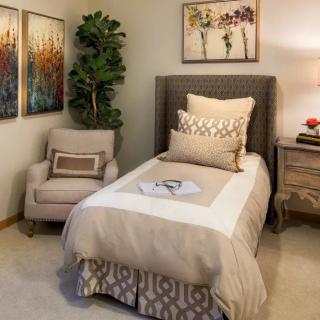 A cozy bedroom with a single bed, decorative pillows, an armchair, and artwork on the walls.