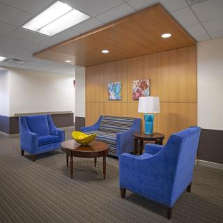 A modern lobby area featuring blue upholstered chairs, a sofa, and a small table with a lamp.