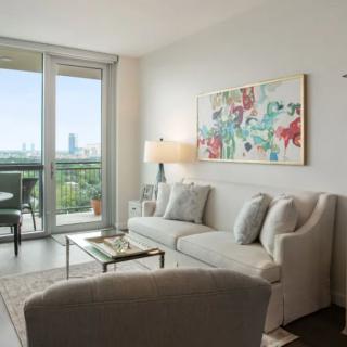 A modern living room with stylish decor, featuring a comfortable sofa, coffee table, and large artwork, opening to a balcony with a city view.