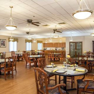 A spacious dining room with neatly arranged tables and chairs, featuring elegant lighting and wooden flooring.