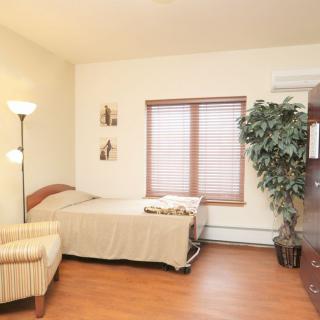 A cozy bedroom featuring a bed, striped armchair, floor lamp, and a large plant by the window.
