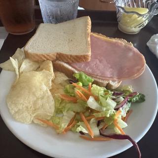 A meal featuring a ham sandwich, salad, and potato chips on a plate.