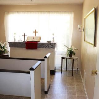 A small chapel interior featuring an altar with crosses and pews.