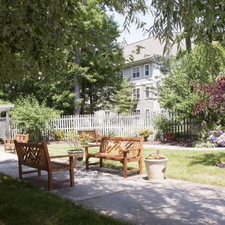 A tranquil garden setting with wooden benches and chairs on a sunlit path.