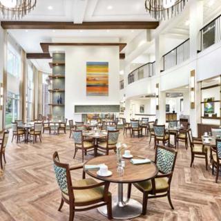 A spacious and elegantly designed restaurant interior with modern decor, showcasing multiple tables and chairs under high ceilings adorned with chandeliers.