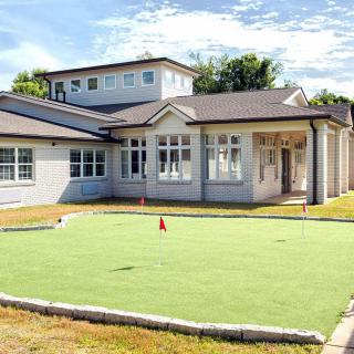 A modern house with a golf putting green in the front yard.